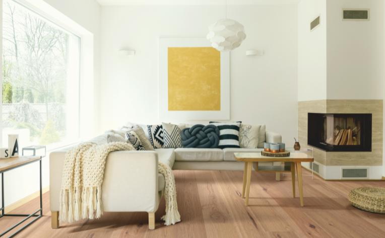 warm toned hardwood flooring in living room with cream couch, fireplace, and lighting.